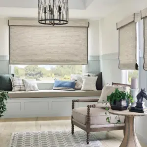 Woven wood shades over a bay window seat with pillows, under a chandelier, beside an upholstered armchair