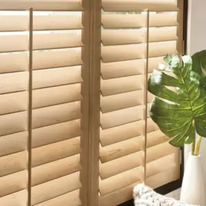 Close-up of natural wood plantation shutter louvers beside a large monstera leaf