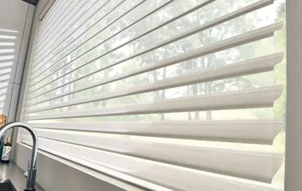Sheer roller shade filtering light through a kitchen window above the sink, with trees visible outside